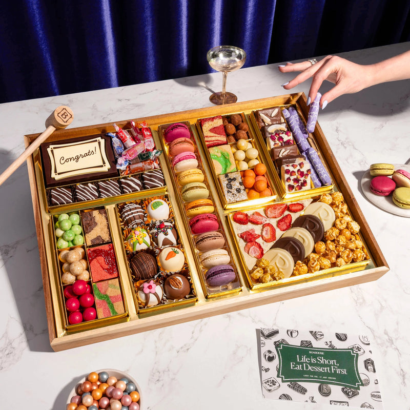 Assorted chocolates in a wooden box on a white surface with a blue curtain background.