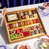 Assorted chocolates in a wooden box on a marble surface with a hand holding a glass.
