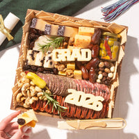 A small graduation cheese board featuring 'GRAD' and '2026' cheese letters alongside salami, cheeses, nuts, and chocolate-covered almonds.