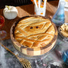 Halloween-themed baked brie in a wooden tray decorated to look like a mummy on a wooden board.
