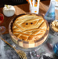 Halloween-themed baked brie in a wooden tray decorated to look like a mummy on a wooden board.
