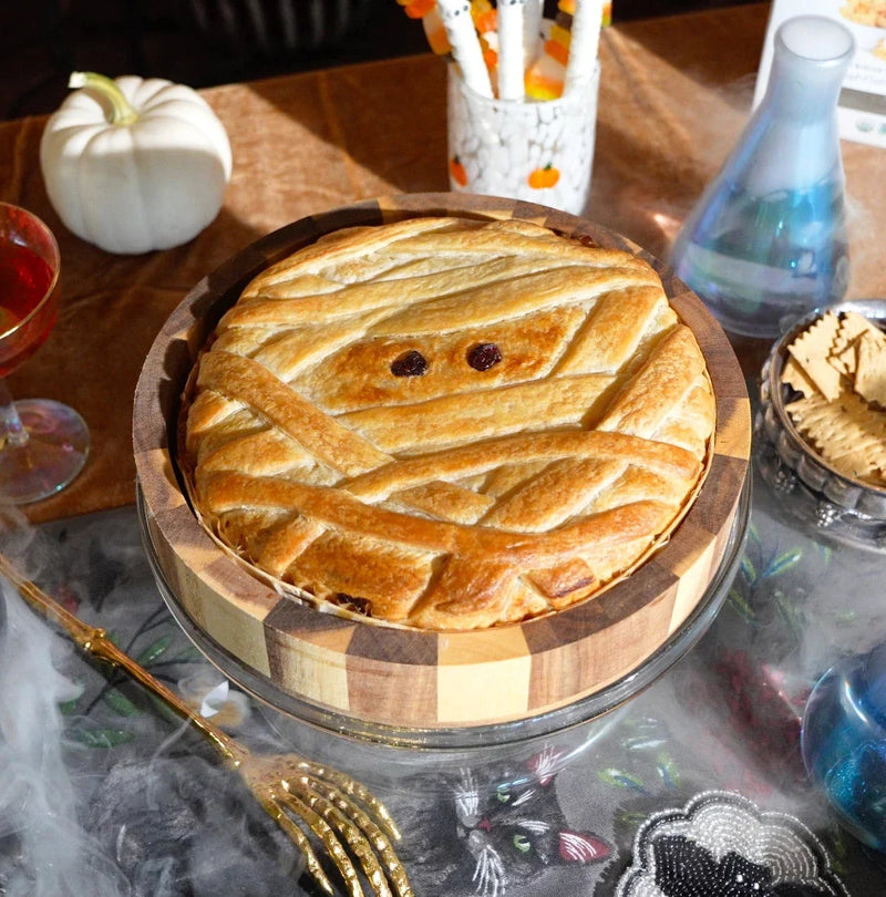 Halloween-themed baked brie in a wooden tray decorated to look like a mummy on a wooden board.