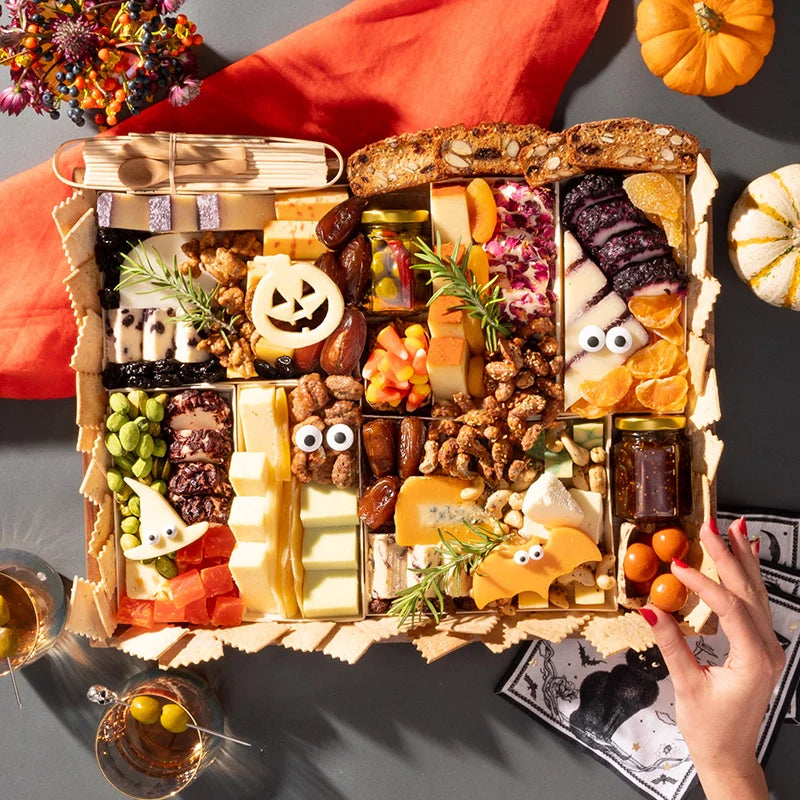 Halloween-themed charcuterie board featuring festive cheeses shaped like a pumpkin and bat, surrounded by assorted snacks and decorations.