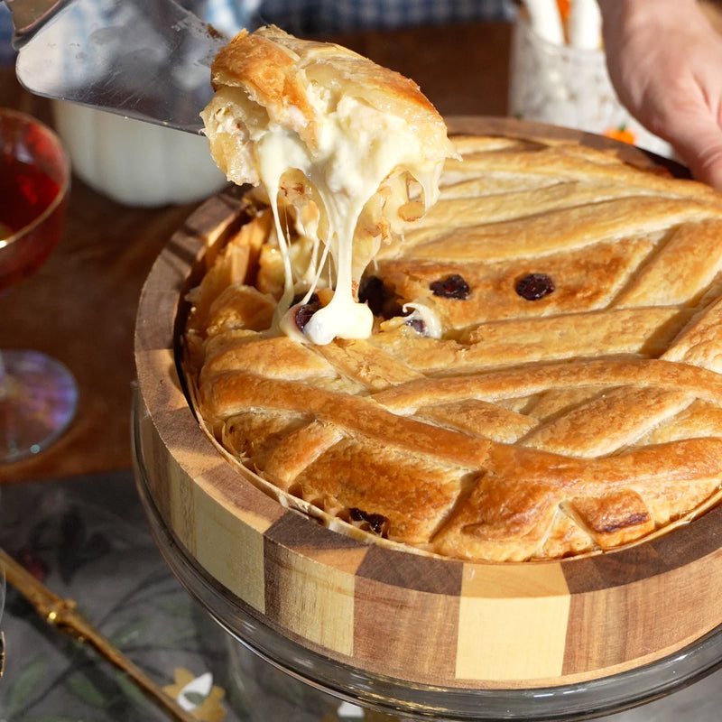 Cheesy baked brie slice being lifted from a wooden bread board with strings of cheese.