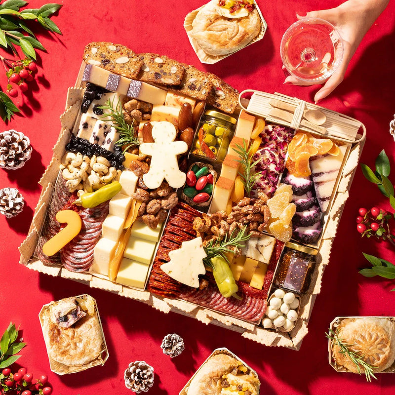 Holiday food spread arranged as a vibrant festive charcuterie board with assorted cheeses, meats, nuts, fruits, and seasonal garnishes.