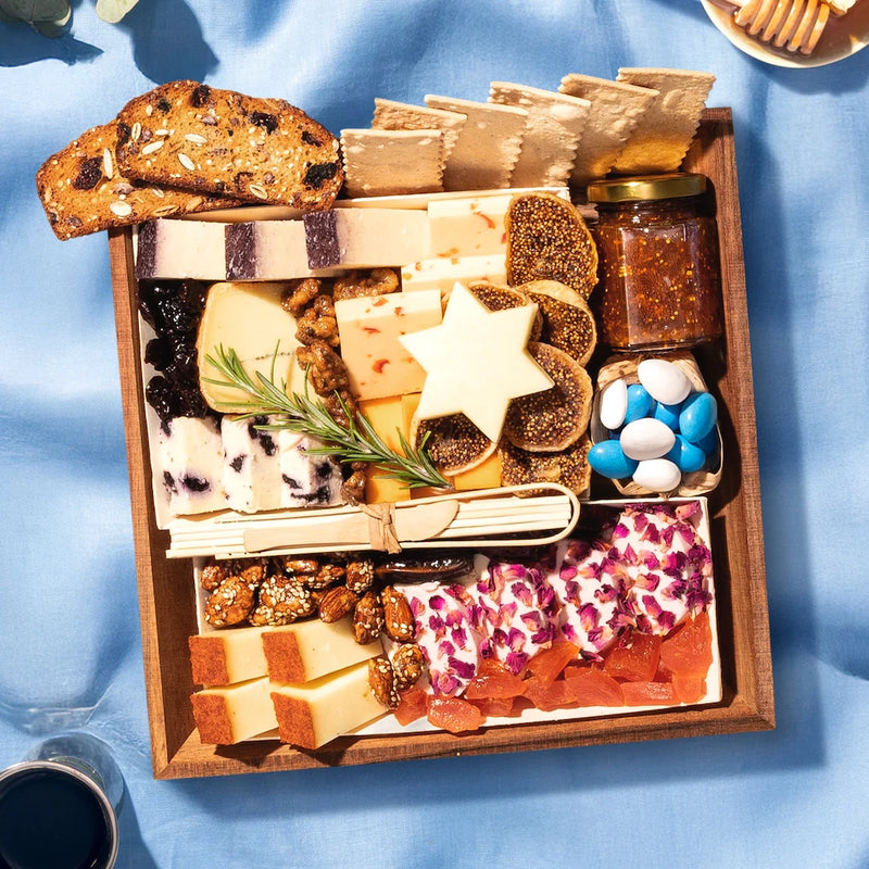 jewish holiday themed cheese board with various cheeses, crackers, and accompaniments on a blue surface.