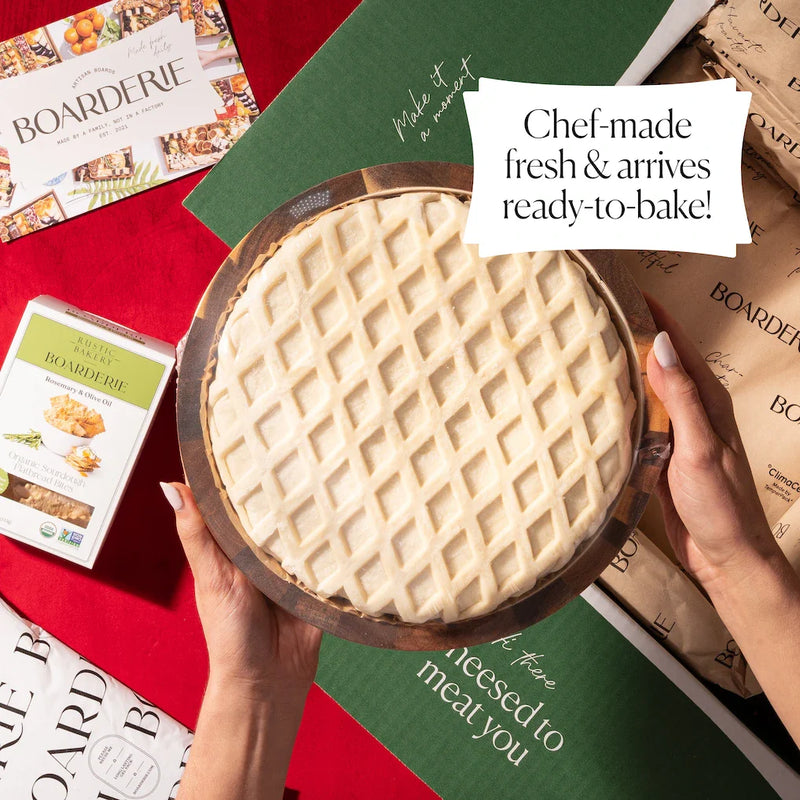Ready-to-bake holiday brie with lattice crust, shown in packaging with Boarderie branding on a festive table.