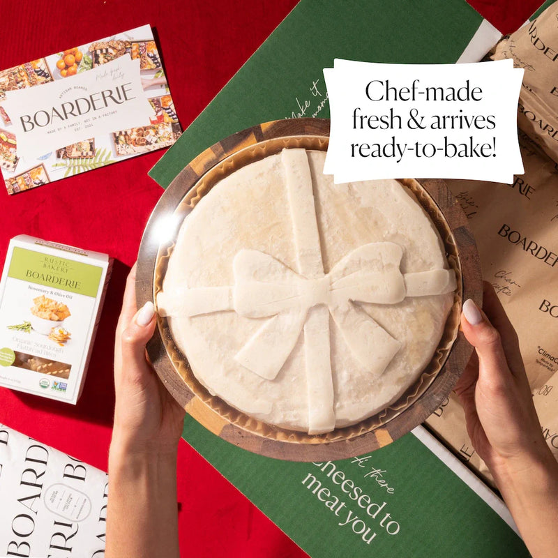 Ready-to-bake holiday brie shaped like a gift with a bow, displayed with Boarderie packaging on a festive background.