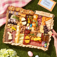 A large easter charcuterie board featuring cheeses, meats, crackers, nuts, and festive egg and bunny-shaped treats on a picnic setup.