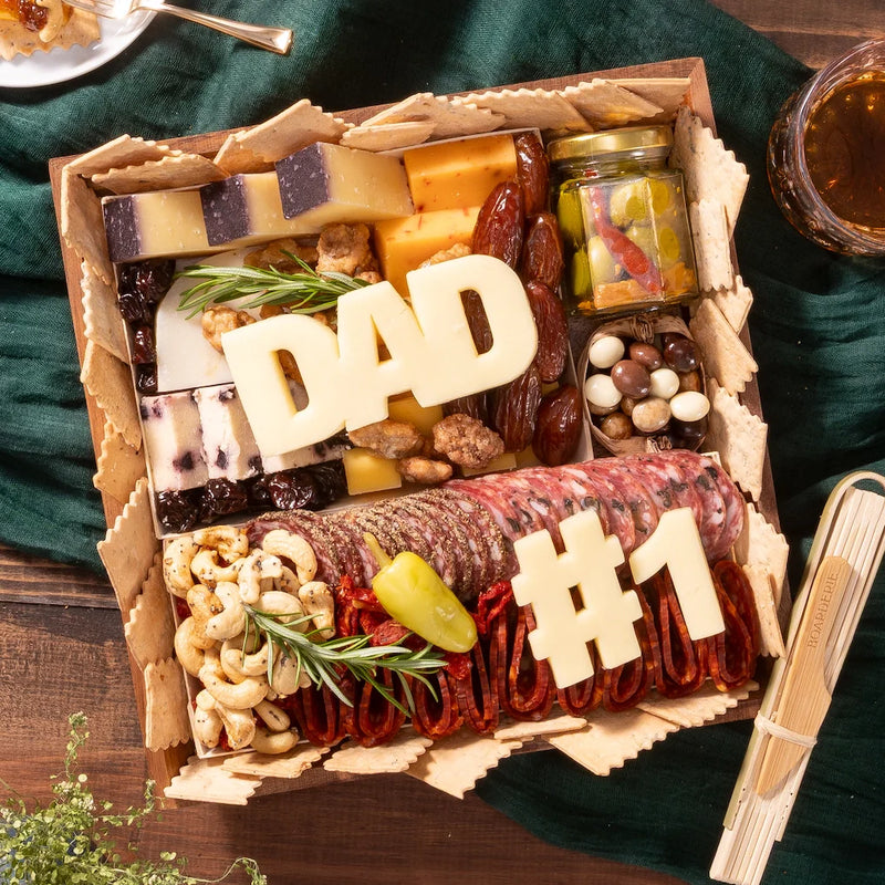 Charcuterie board for Father’s Day featuring meats, cheeses, nuts, pickles, and cheese cutouts spelling “DAD” and “#1”.