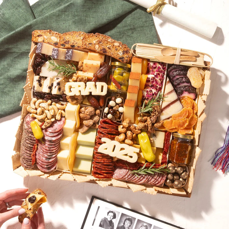 Charcuterie board for graduation party featuring meats, artisan cheeses, fruits, and celebratory cheese cutouts labeled “GRAD” and “2025.”