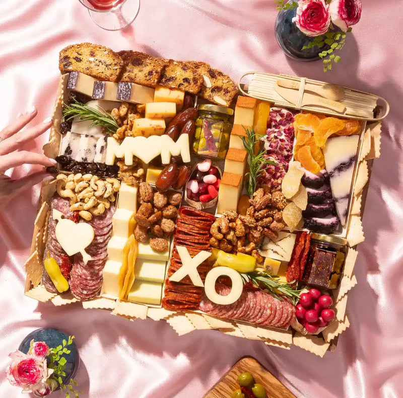Large Mother's Day charcuterie board with meats, cheeses, dried fruits, nuts, and "MOM" and "XO" cheese cutouts.