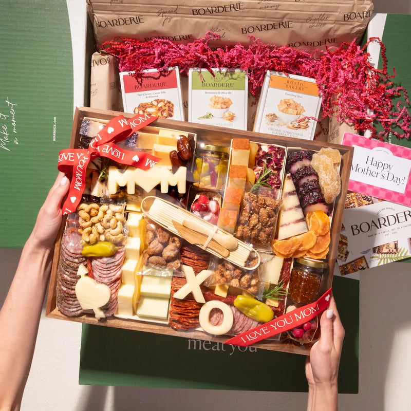 Mother's Day charcuterie delivery box featuring meats, cheeses, treats, and "MOM" and "XO" cheese cutouts with festive packaging.