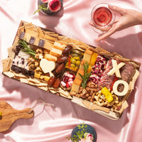 Valentine’s Day charcuterie board with artisan cheeses, meats, nuts, heart-themed cheese cutouts, and red ribbon on a pink tablecloth.