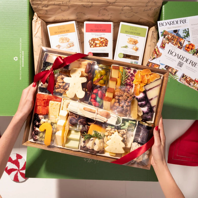 Christmas cheese board with festive tree and gingerbread-shaped cheeses, nuts, dried fruits, and crackers in a holiday gift box.