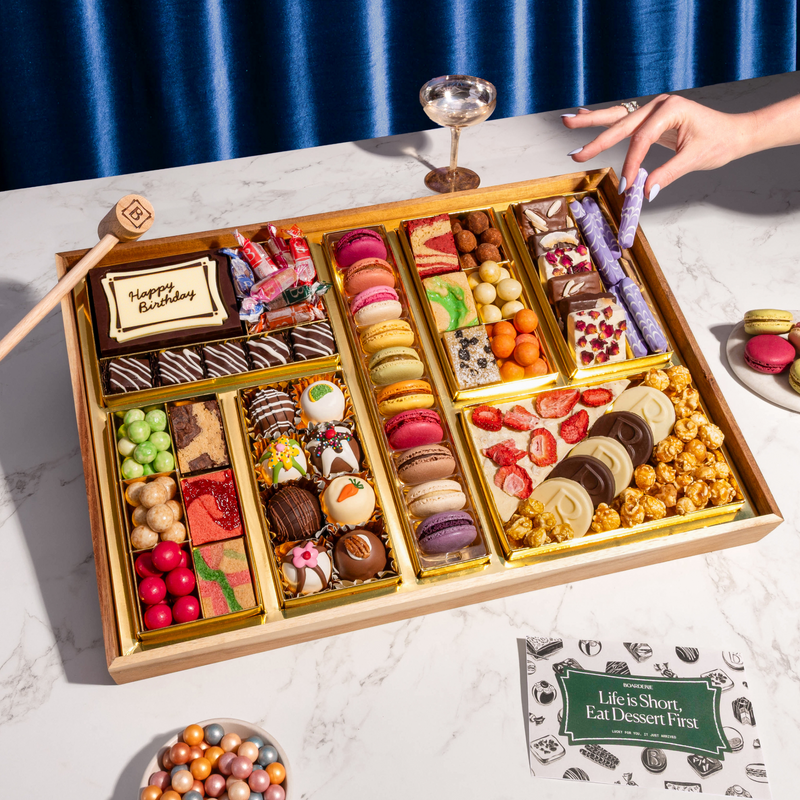 Large dessert gift box with "Happy Birthday" chocolate card, macarons, bonbons, chocolate-covered berries, fresh strawberries, popcorn, and candies on marble surface