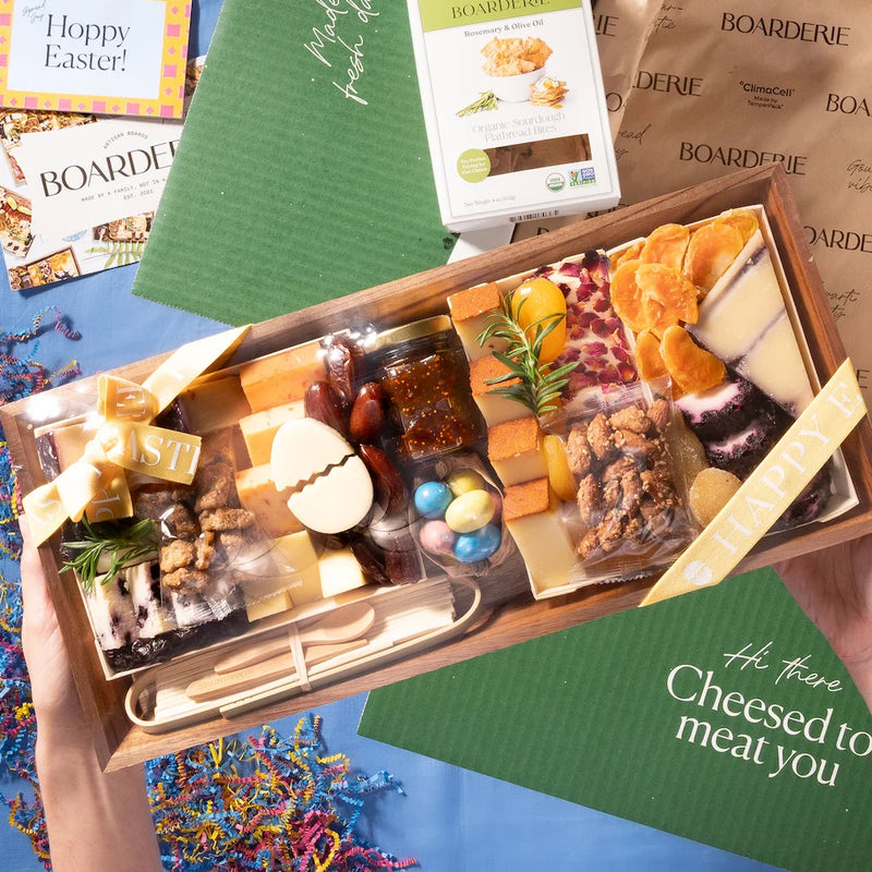 Easter charcuterie board with assorted cheeses, nuts, dried fruits, fig jam, and a festive egg-shaped cheese cutout.