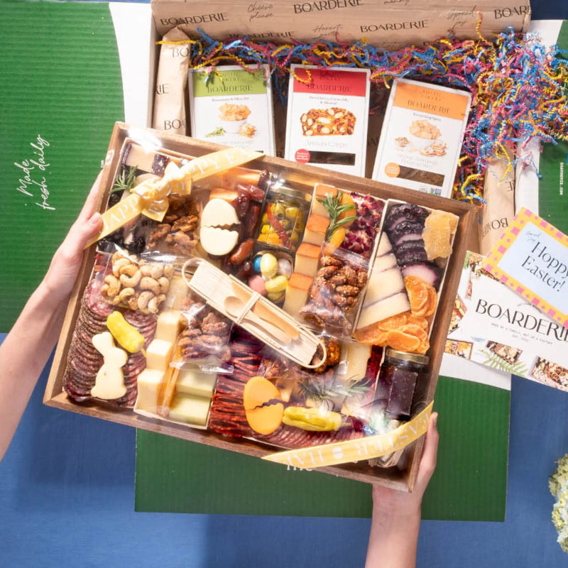 An Easter cheese board being unboxed, featuring bunny-shaped cheeses, crackers, cured meats, nuts, and honey arranged in a gift box with Boarderie packaging.