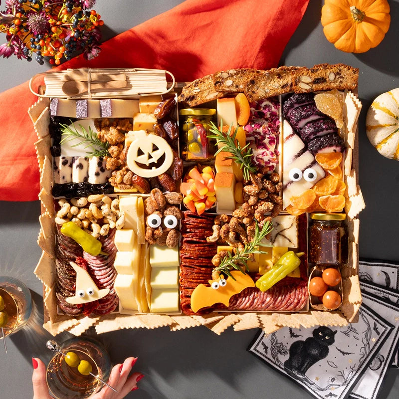 Halloween-themed charcuterie board featuring festive cheeses shaped like a pumpkin and bat, surrounded by assorted snacks and decorations.