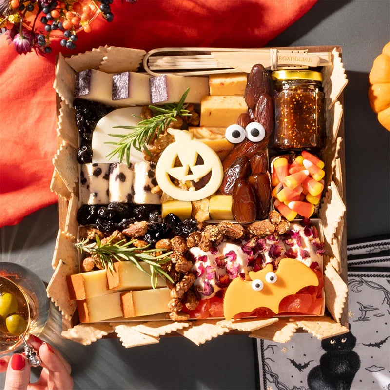 Halloween-themed cheese board with festive cheese shapes, figs, candy corn, nuts, and a small jar of fig jam, arranged without any meats