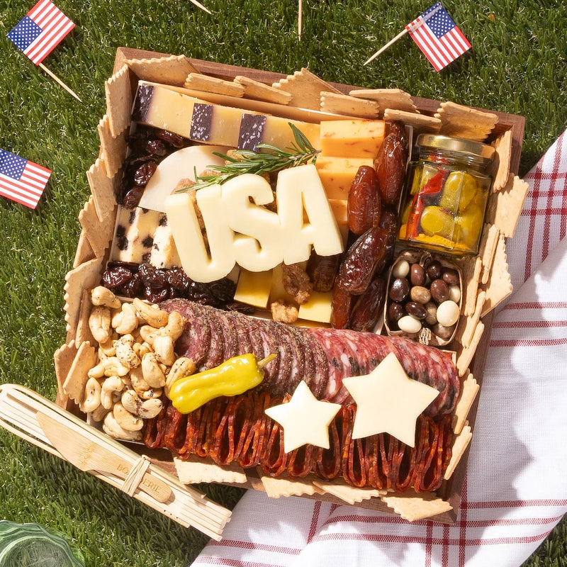 4th of July charcuterie board with meats, cheeses, nuts, and patriotic cheese cutouts spelling “USA” and shaped like stars.