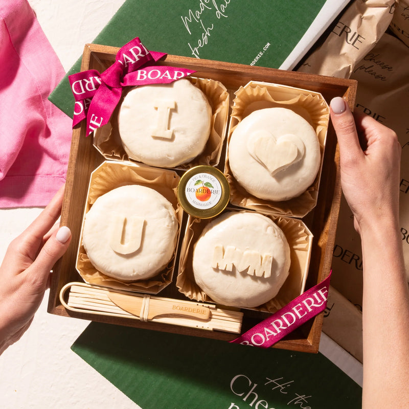 Mother’s Day cheese board featuring four brie wheels with carved messages saying I love you mom and fig marmalade.