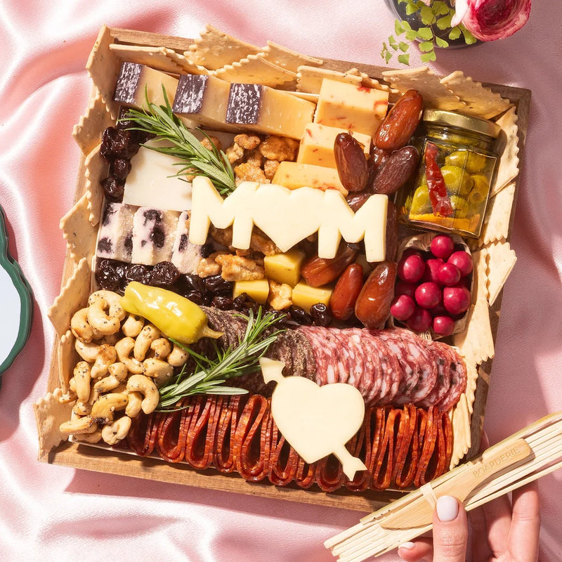 Mother’s Day brunch charcuterie board with cheeses, meats, nuts, fruit, and cheese cutouts shaped like “MOM” and a heart.