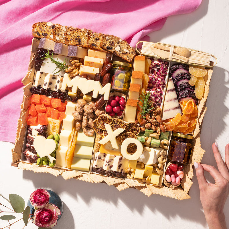 Mother's Day cheese board with assorted cheeses, dried fruits, nuts, and "MOM" and "XO" cutouts in cheese.
