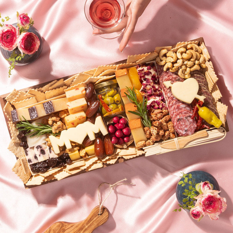 Charcuterie board for Mother’s Day with meats, cheeses, nuts, dried fruits, and cheese cutouts shaped like “MOM” and a heart.