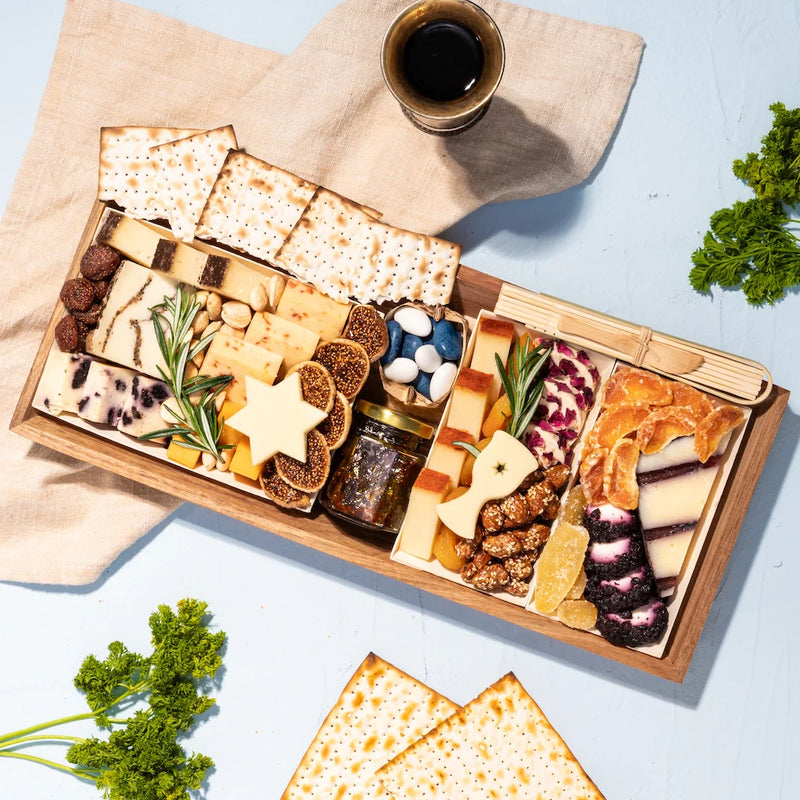 Passover charcuterie board with matzo, artisanal cheeses, dried fruits, nuts, fig jam, and star-shaped cheese cutouts.