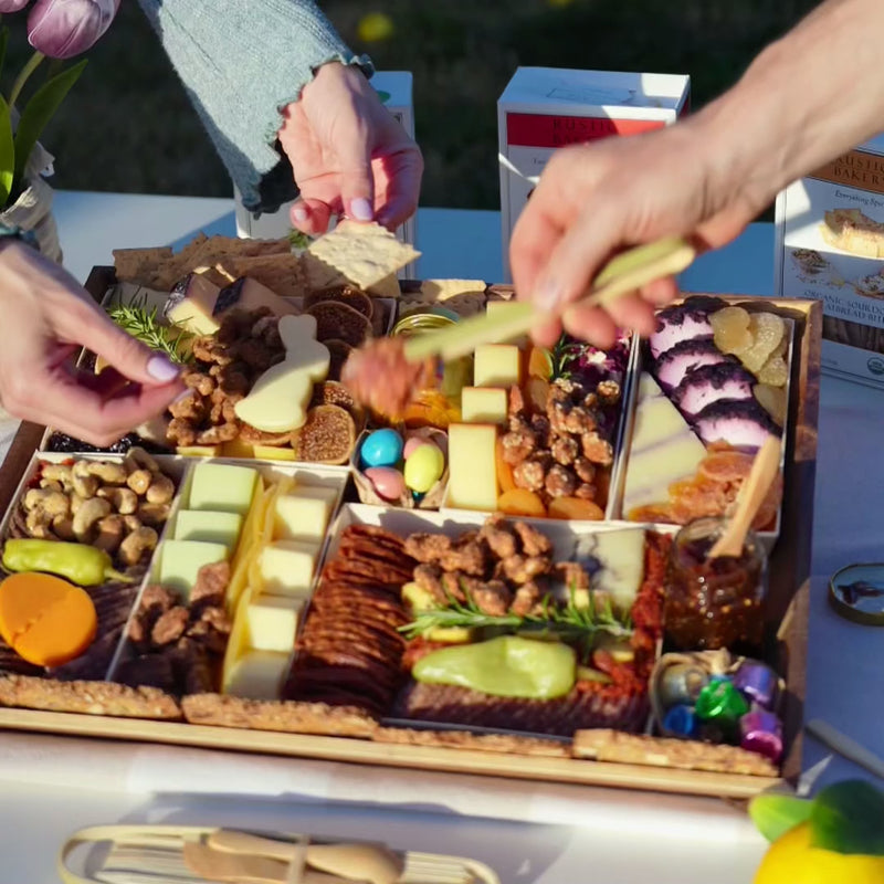 Charcuterie board for Easter with cheeses, meats, nuts, dried fruits, fig jam, and festive egg and bunny cheese shapes.