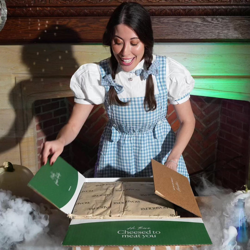 video of girl unboxing a frozen baked brie with mummy decoration on the pastry. Baked brie is baked in the over and cut open on a halloween themed table.
