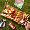 Super Bowl charcuterie board featuring cheeses, meats, crackers, nuts, and football-themed cheese cutouts on a picnic setting.