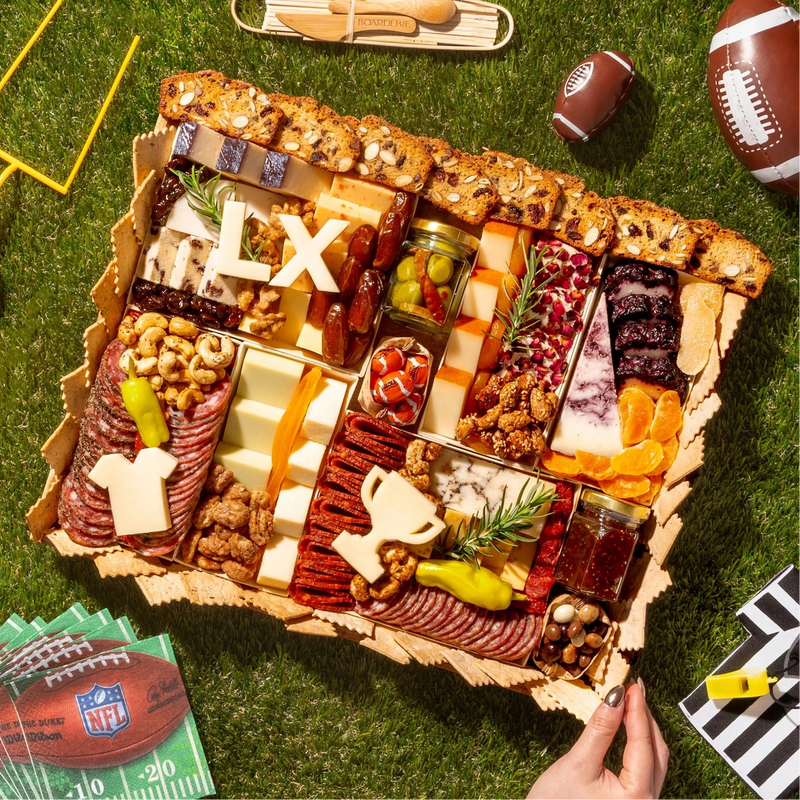 Super Bowl charcuterie board with gourmet cheeses, meats, nuts, and cheese cutouts shaped like a helmet, jersey, and “LX.”