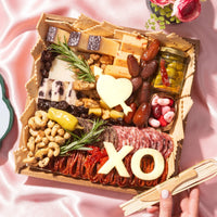 Valentine’s Day cheese board with artisan cheeses, cured meats, nuts, olives, and romantic cheese cutouts shaped like a heart and XO.