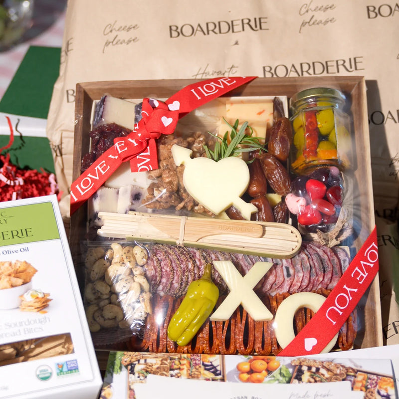 Charcuterie for Valentine’s Day featuring artisan meats, cheeses, nuts, pickled vegetables, and heart and XO-shaped cheese cutouts with love-themed ribbon.