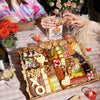 Valentine’s charcuterie board with heart-shaped cheeses, meats, fruits, and nuts on a pink checkered tablecloth.