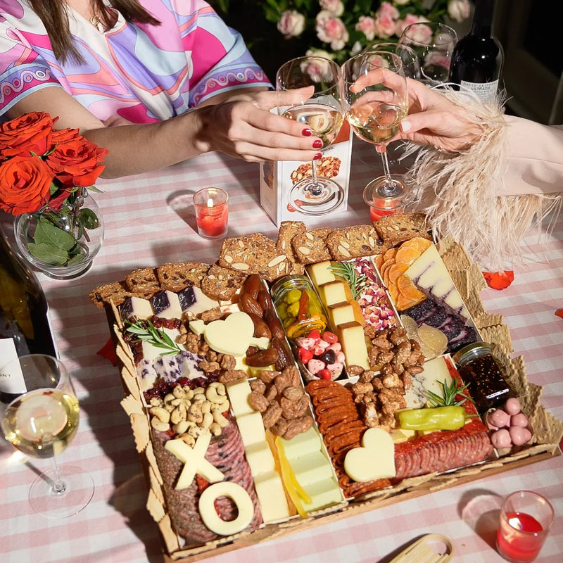 Valentine’s charcuterie board with heart-shaped cheeses, meats, fruits, and nuts on a pink checkered tablecloth.